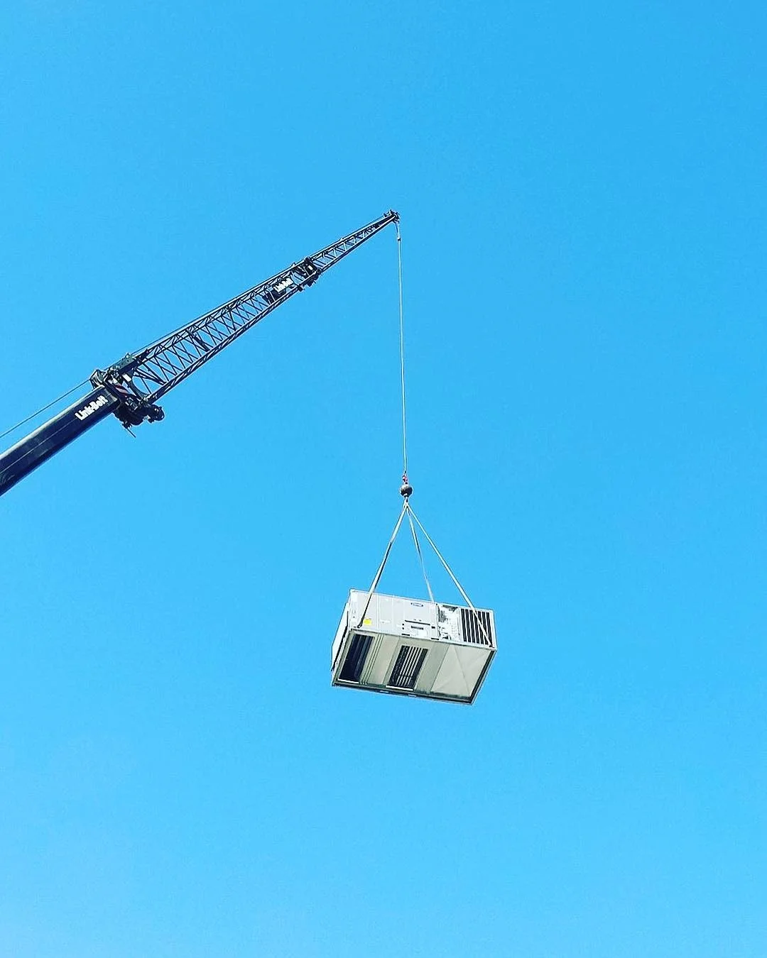Commercial HVAC rooftop unit suspended by crane with rigging straps during installation