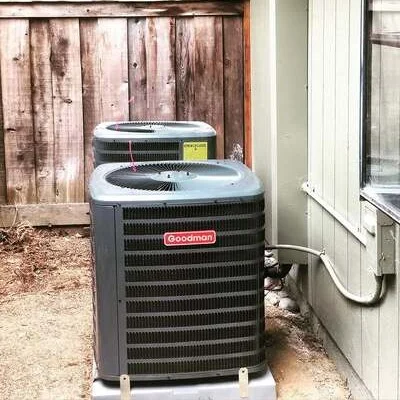 Two Goodman AC condenser units installed on concrete pads against exterior wall
