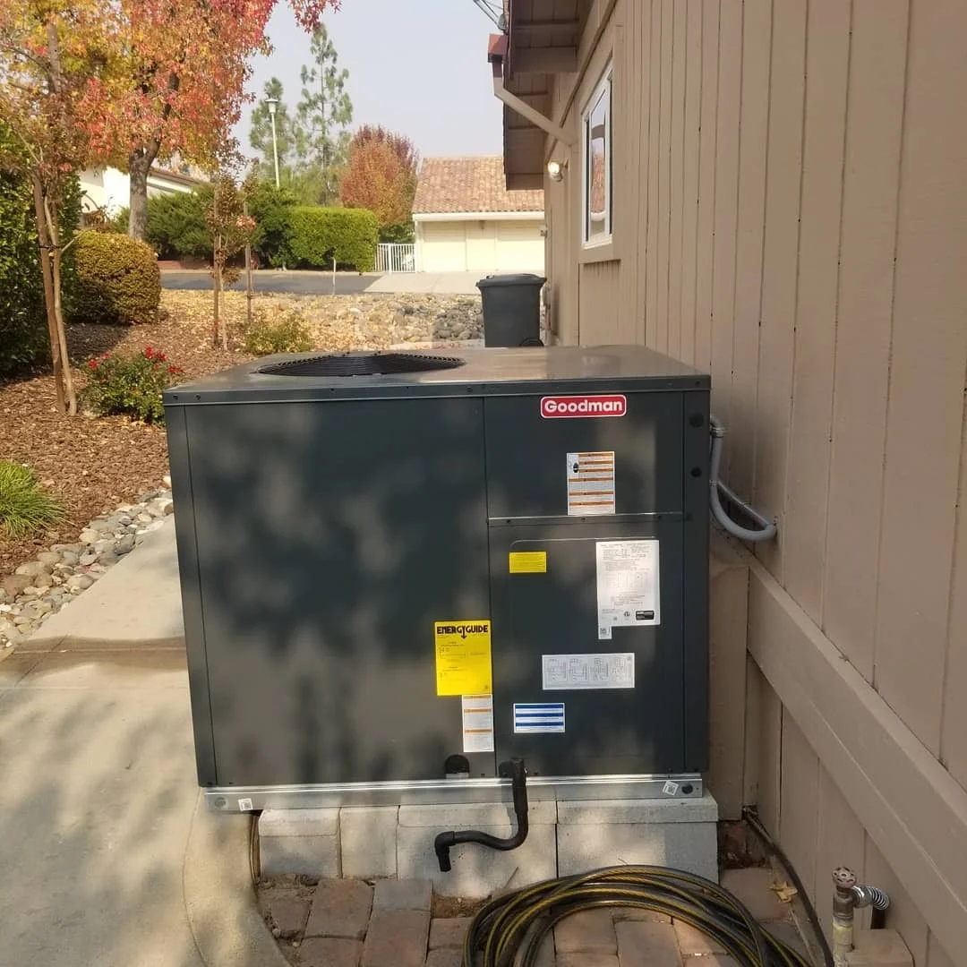 Goodman air conditioning condenser unit installed on concrete pad with electrical connections and refrigerant lines