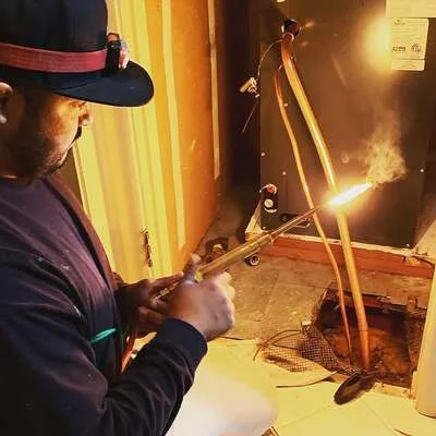 Technician welding metal ductwork sections with support frame and bright welding arc visible