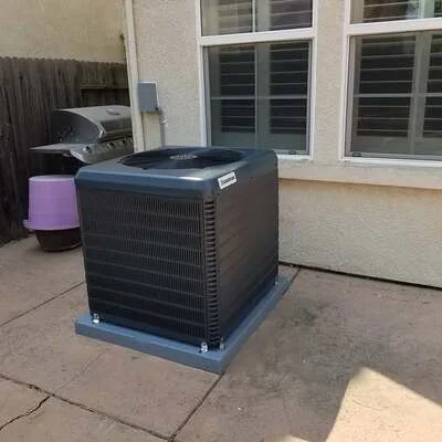 Black AC condenser unit on concrete pad beside residential home with stucco exterior