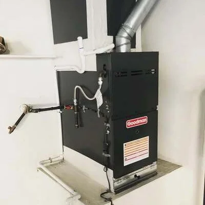 Black gas furnace with metal ductwork and white PVC venting installed on concrete pad