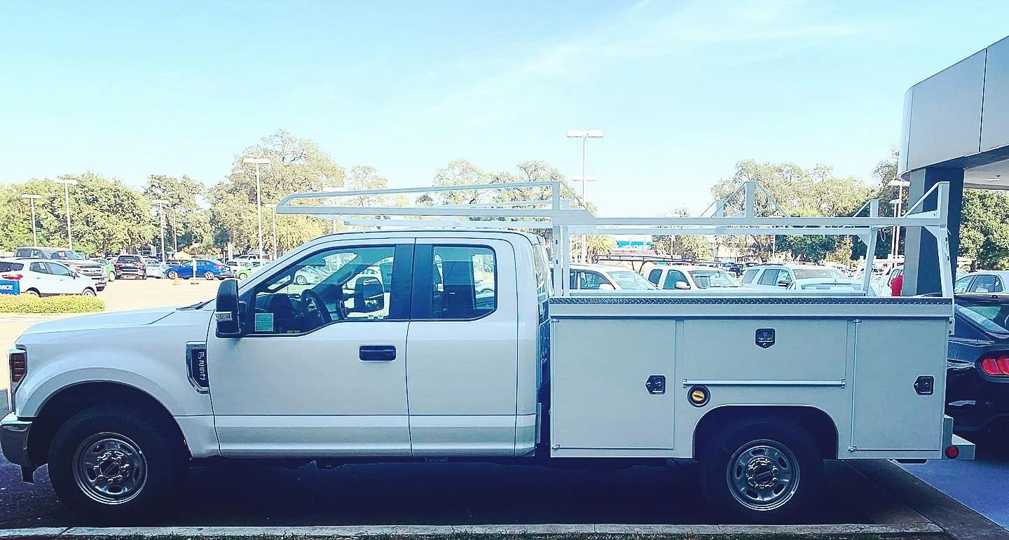 White service truck with overhead rack and enclosed storage bed for HVAC equipment transport